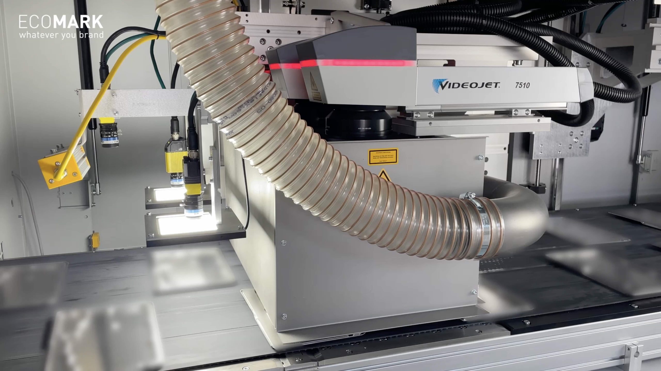 Nahaufnahme einer industriellen Druckausrüstung mit einem großen flexiblen Schlauch, der mit VIDEOJET 7510 beschriftet ist. Die Maschine steht in einem sauberen, hellen Arbeitsbereich und trägt das ECOMARK-Logo in der oberen linken Ecke. eco-mark ecomark laserkennzeichnung laserbeschriftung industrie
